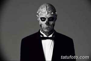 Фото тату: мужчина с татуировкой черепа на лице, в смокинге и с украшением на голове. Детализированный рисунок, черно-белая гамма.